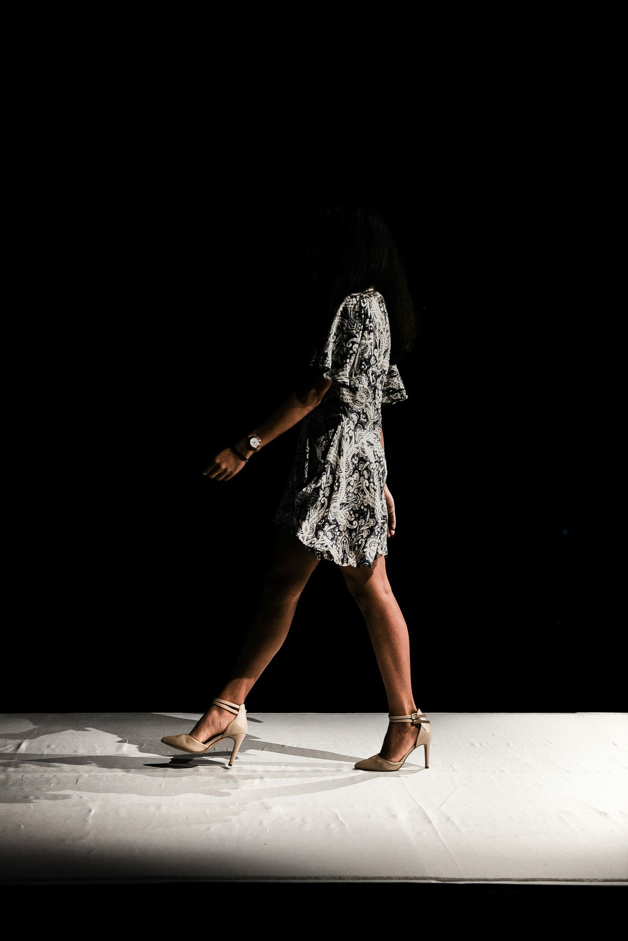 woman wearing black and white floral dress walks inside dark room